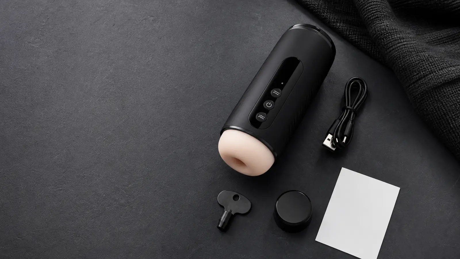 A compact automatic wellness device with charging cable, lock accessory, cap, and a plain guide card on a charcoal surface.