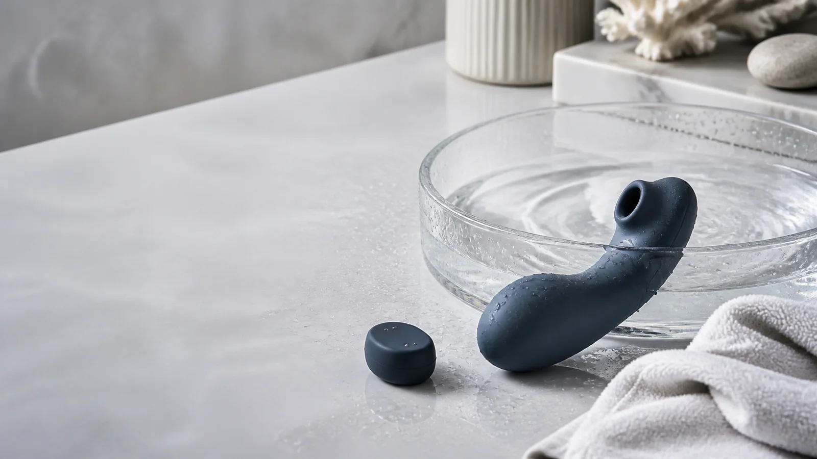 A waterproof personal wellness device beside a rinse bowl, drying towel, and dry charging cap.